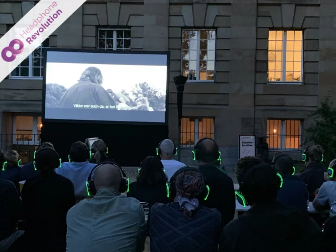 Menschen tragen spezielle Silent Kopfhörer bei einem Outdoor Silent Cinema vor der Staatsoper in Stuttgart.