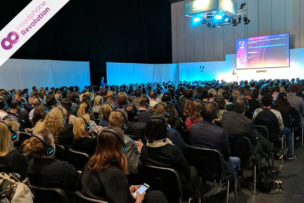 Viele sitzende Menschen, die auf der Adobe Summit Konzerenz einem Panel zuhören und Kopfhörer tragen, über die der Ton von der Stage übertragen wird.