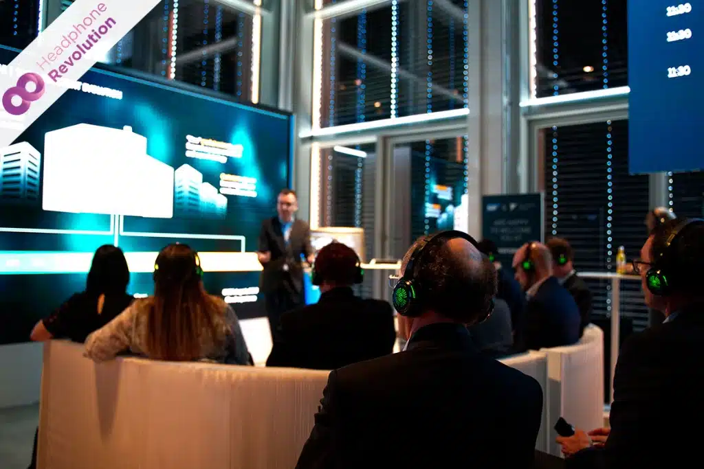 Ein Unternehmer hält einen Vortrag in einem Konzerenzraum, bei dem der Ton über Silent Conference Kopfhörer von Headphone Revolution zu hören ist.