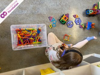 Ein Kind baut auf dem Boden mit magnetischen Spielsteinen und tragt dabei Silent Education Kopfhörer von Headphone Revolution und sich besser zu konzentrieren.