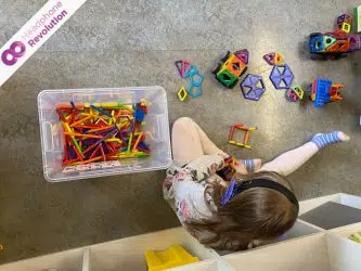 Ein Kind baut auf dem Boden mit magnetischen Spielsteinen und tragt dabei Silent Education Kopfhörer von Headphone Revolution und sich besser zu konzentrieren.