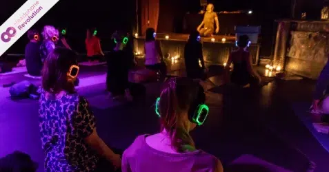 Viele Menschen machen Yoga und tragen dabei Silent Fitness Kopfhörer von Headphone Revolution auf welchen der Ton übertragen wird.