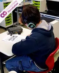 Ein Schüler trägt leuchtende Silent Kopfhörer im Unterricht und füllt dabei ein Arbeitsblatt aus.