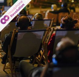 Mehrere Menschen sitzen auf Liegestühlen und nutzen bei einem Silent Cinema in Berlin die Silent Kopfhörer von Headphone Revolution, um den Ton zu hören.