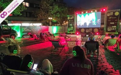Bei einem Silent Concert Livestream schauen die Teilnehmer ein Konzert auf einer Leinwand während sie den Ton über spezielle Silent Kopfhörer von Headphone Revolution hören.