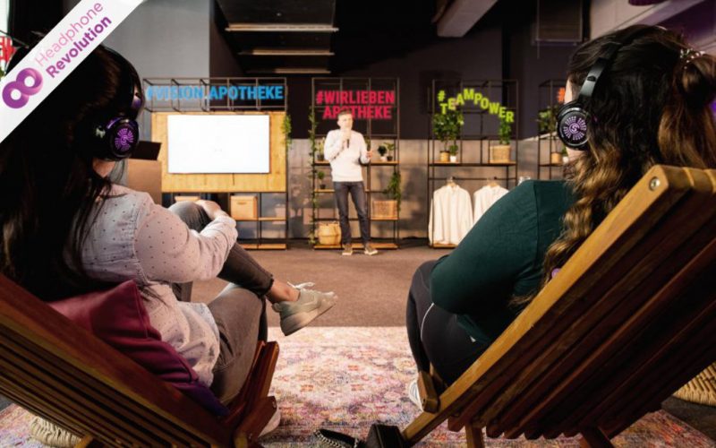 Zwei Frauen hören einem Speaker zu und tragen dabei Silent Conference Kopfhörer über die der Ton übertragen wird.