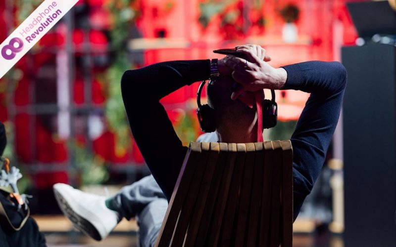 Ein Besucher einer Messe sitzt auf einem Liegestuhl und trägt einen Silent Conference Kopfhörer auf den der Ton eines Redners übertragen wird.