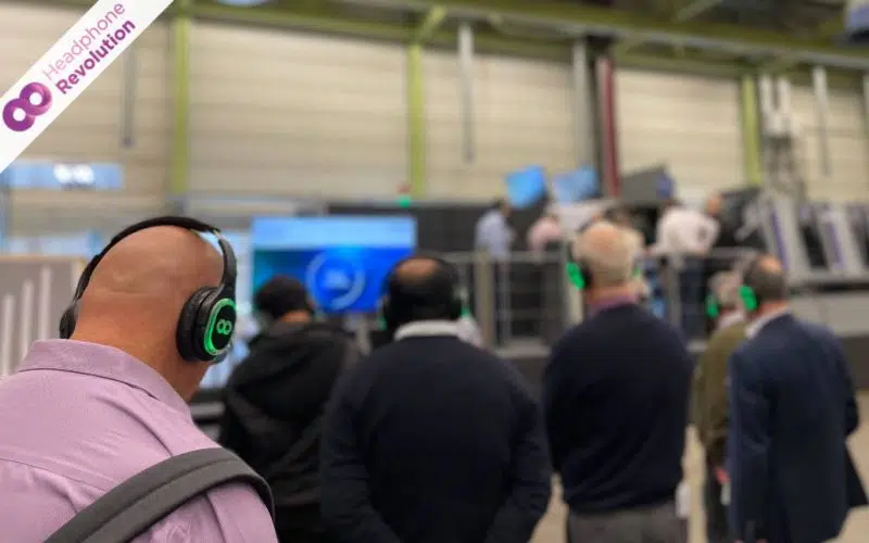 Bei einer Betriebsführung durch eine Druckmaschinenfabrik tragen die Teilnehmer spezielle Silent Conference Tour Guide Kopfhörer von Headphone Revolution, um den Ton einwandfrei verstehen zu können, trotz der lauten Umgebungsgeräusche.