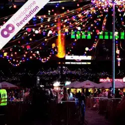 Einige Menschen feiern bei einer Silent Disco von Clubs United in Essen auf dem Kennedyplatz und hören unter bunten Licherketten die Musik über die leuchtenden Silent Disco Kopfhörer von Headphone Revolution.