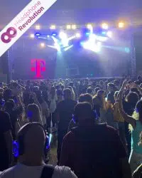 Sehr viele Telekom Mitarbeiter feiern ihr Mitarbeiterfest vor einer Bühne mit den lila leuchtenden Silent Disco Kopfhörern von Headphone Revolution und einer Silent Disco.