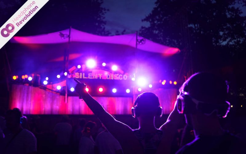 Einige Leute feiern ausgelassen vor einer Bühne auf dem Happiness Festival zu einer Silent Disco mit den Silent Dico Kopfhörern von Headphone Revolution.