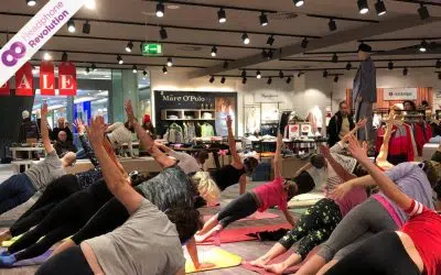 Bei einem Silent Yoga Event in einem Einkaufszentrum tragen die Teilnehmer spezielle Silent Disco Kopfhörer, um die Anweisungen der Yoga Lehrerin zu verstehen.