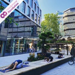 Teilnehmerinnen eines Silent Yoga Kurses machen Outdoor Übungen und tragen dabei Kopfhörer von Headphone Revolution über die der Ton der Yogalehrerin übertragen wird.