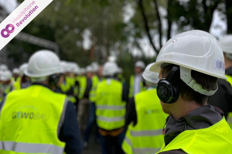 Ein Silent Conference Kopfhörer von Headphone Revolution wird von einem Mann unter seinem Sicherheitshelm getragen, damit er den Ton der Baustellenführung zu hören kann.