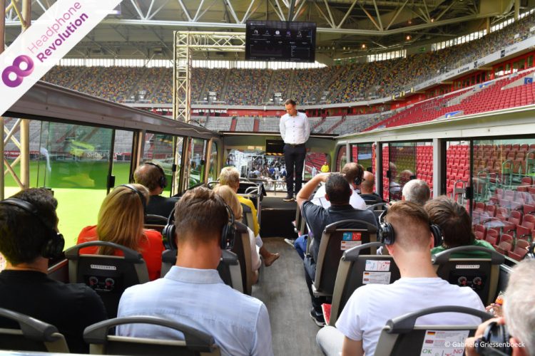 Ein Mann hält einen Vortrag im Stadion in Düsseldorf, bei dem die Teilnehmer spezielle Silent Conference Kopfhörer tragen, um ihn besser zu verstehen.