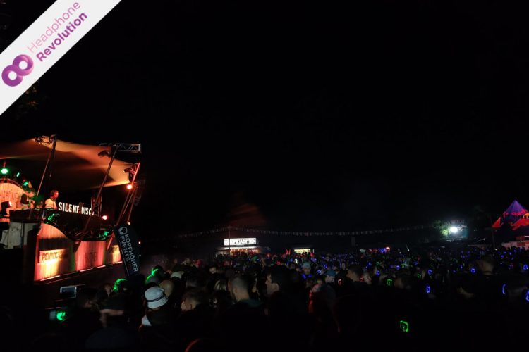 Die DJs einer Silent Disco und die Menge an Menschen vor der Bühne feiern gemeinsam auf einem Festival, bei dem die Musik über die Kopfhörer von Headphone Revolution abgespielt wird.