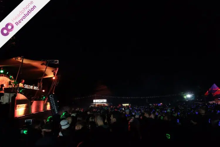 Die DJs einer Silent Disco und die Menge an Menschen vor der Bühne feiern gemeinsam auf einem Festival, bei dem die Musik über die Kopfhörer von Headphone Revolution abgespielt wird.