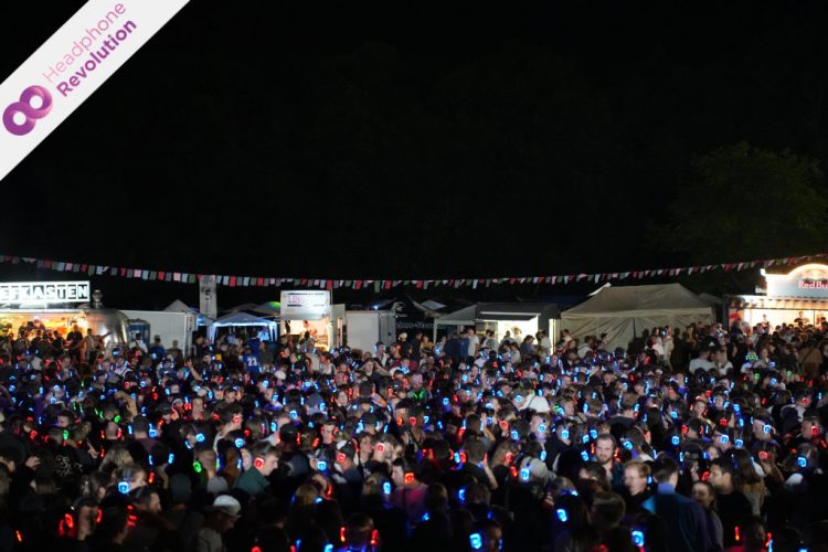 Tausende Menschen tragen im Publikum verschieden farbig leuchtende Kopfhörer auf einer Silent Disco auf einem Festival.
