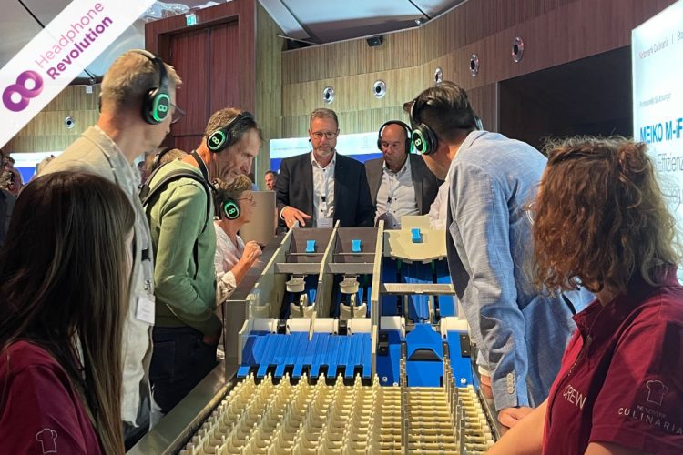 Ein Sprecher einer Silent Conference erklärt den Besuchern über HRT12PRO Kopfhörer ein Modell